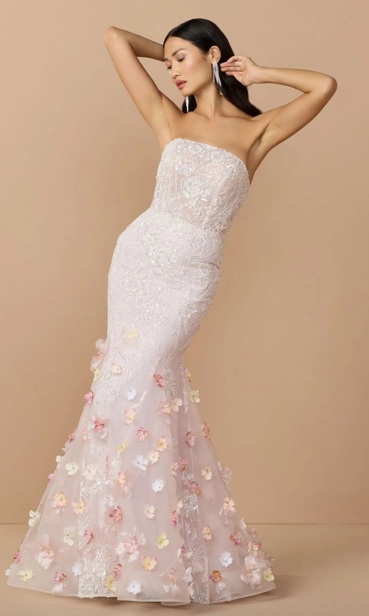 Woman in the Mac Duggal 21147 Long Formal Dress in Blush Multi—strapless with floral appliques and a mermaid silhouette—poses elegantly with one arm raised against a beige background, capturing the embellished mesh gown trend.